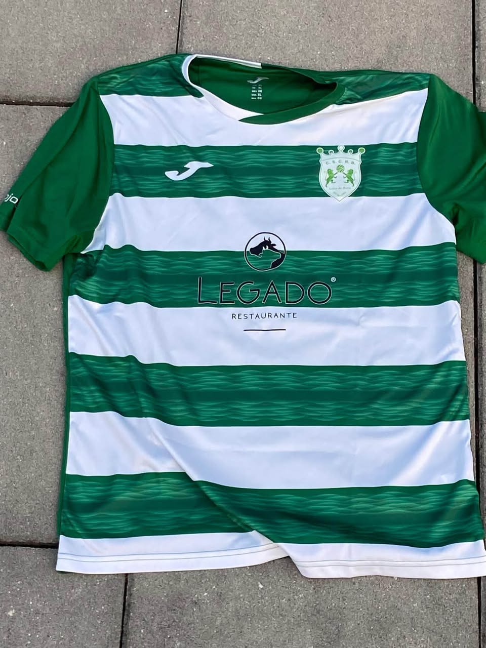 Camisola verde e branca dos Leões da Beira, com o emblema do clube e o patrocínio do Restaurante O Legado.
